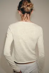 Camiseta slim fit de algodón color crudo, con cuello redondo, manga larga y cierre frontal de múltiples botones pequeños.