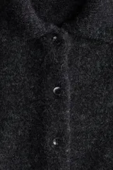 Saco de punto suave color gris oscuro, con cuello camisero y botones frontales. Presenta un diseño de hombros caídos y mangas holgadas que terminan por debajo del codo.