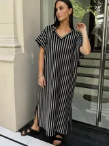 Vestido largo de tejido de punto con diseño de rayas verticales en blanco y negro. Presenta escote en V, mangas cortas y tajos laterales en el ruedo para mayor movimiento.