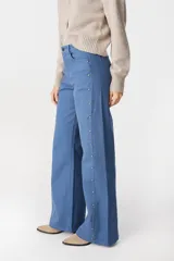 Jean de corte recto y tiro medio, color azul, con detalles de tachas metálicas doradas a lo largo de las costuras laterales externas.