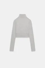 Sudadera crop entallada de color negro, con cuello alto, manga larga y cierre frontal de cremallera metálica. Presenta un diseño corto con bajo asimétrico.