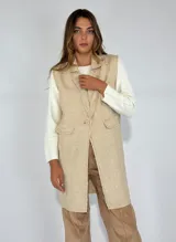 Chaleco largo color beige, con cuello solapa, un botón frontal y dos bolsillos de parche. Presenta costuras decorativas en contraste.