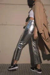 Pantalón de ecocuero metalizado color plateado, de corte capri semi oxford y tiro medio-alto. Presenta cierre frontal con botón metálico y costura horizontal a la altura de la rodilla.
