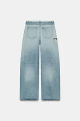 Jeans de mezclilla de tiro medio, corte wide leg y diseño relaxed. Presenta detalles rotos y desgastados en las piernas, y una cinturilla doblada superpuesta con trabillas y cierre frontal con cremallera y botón metálico.