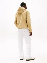 Cortavientos color beige de corte amplio, con capucha fija, cierre de cremallera, dos bolsillos delanteros con cremallera, forro con diseño integral de la insignia de Tommy y parche de Tommy en el pecho.