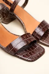 Sandalia de cuero vacuno color negro con textura de cocodrilo, taco cuadrado de 4 cm, punta cuadrada y dos tiras finas, una en el empeine y otra con hebilla en el tobillo.