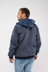 Campera de nylon color azul marino con cierre frontal completo, capucha desmontable y puños elásticos. Presenta bolsillos con cierre y logo aplicado en la manga.