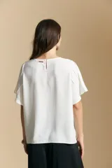 Top de color azul, con escote redondo a la base y mangas cortas amplias con caída fluida. Presenta una silueta relajada y un diseño minimalista.