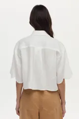 Camisa crop blanca de lino con silueta relajada, cuello clásico y mangas cortas. Presenta bordados de tigres en el frente y detalles ornamentales en los hombros.