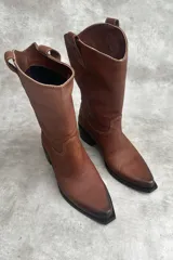 Botas de cuero vacuno color negro, de caña media con bordado a contratono, tacón bajo, punta alargada redondeada y suela cuadrada lisa.