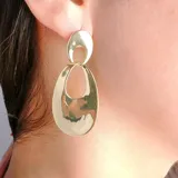 Aros colgantes dorados con diseño de dos óvalos interconectados, uno sólido y otro con abertura.