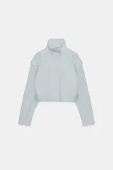 Chaqueta corta de cuello subido con manga larga, cierre frontal con cremallera y botones a presión ocultos. Presenta bolsillos delanteros y puños con pliegues.