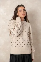 Buzo de punto color beige con estampado de lunares negros en relieve, cuello redondo y mangas largas con puños acanalados.