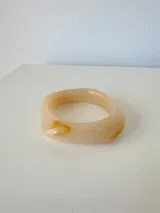 Pulsera rígida de acrílico con diseño asimétrico y acabado marmolado en tonos beige y tostado.