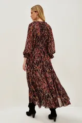 Vestido midi de corte holgado con estampado ikat en tonos bordó y tierra. Presenta cuello redondo con lazos, mangas largas abullonadas con puños elásticos y falda con volados escalonados. Incluye un cinturón ancho de estilo rústico con tachas y flecos.