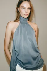 Top halter de cuello subido y hombros descubiertos, confeccionado en tejido fluido con diseño asimétrico y bajo con volantes. Cuenta con cierre en el cuello.