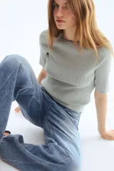 Remera de punto acanalado gris claro, de ajuste entallado con mangas raglán cortas y cuello redondo. Presenta detalles en pointelle y remates acanalados en escote, mangas y bajo.