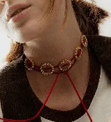 Gargantilla choker con cordón rojo y dijes circulares dorados con strass. El cordón se ata en la parte delantera.