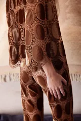 Camisa corta de corte oversize con mangas 3/4, confeccionada en una base de encaje con apliques circulares de terciopelo en tono marrón. Presenta cierre frontal con botones transparentes.