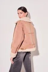 Campera gamulan color rosa con interior de piel sintética color crema, cierre frontal con cremallera y hebillas en el cuello. Corte oversize.