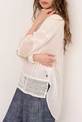 Blusa color blanco, de corte holgado y mangas tres cuartos, con detalles de encaje y bordados en las mangas y en el ruedo.
