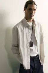 Camisa relaxed fit de algodón con estructura, cuello solapa, manga larga con puño abotonado, bolsillo de parche en el pecho y cierre frontal con botones. Presenta diseño de rayas finas.