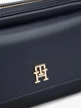 Cartera tipo cámara estructurada de color azul marino, con solapa frontal y logo metálico de Tommy Hilfiger en dorado. Posee un bolsillo externo con cierre de solapa a broche y correa ajustable extraíble.