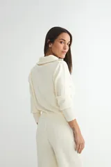 Conjunto de dos piezas tejido en color crema, compuesto por un cárdigan con cierre frontal completo y cuello alto, y pantalón de corte recto con cintura elástica.