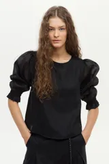 Blusa de lino blanca con escote redondo y mangas cortas abullonadas con detalles de volados en los puños.