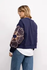 Buzo negro de cuello redondo con diseño de flores bordadas en las mangas. Presenta un corte holgado y puños elásticos.