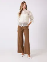 Blusa de tul bordado color beige, marca Liv Los Angeles, con cuello alto, cierre frontal de botones y mangas ¾ amplias con volados.