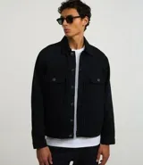 Campera trucker masculina de jeans negro, con cuello inglés, manga larga ajustada, cierre abotonado, bolsillos delanteros y sin estampa.