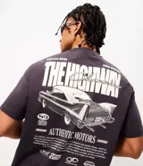 Remera de algodón color gris oscuro con cuello redondo y manga corta. Presenta un diseño gráfico en la espalda con la ilustración de un automóvil clásico, tipografía estilo vintage y detalles decorativos.