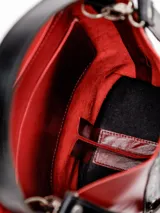 Matera bucket de cuero rojo con detalles en cuero negro y tachas metálicas plateadas dispuestas en líneas diagonales. Cuenta con una manija superior corta.
