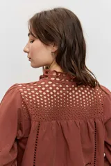 Camisa de manga larga abullonada color marrón, con detalles de bordados calados en el pecho y las mangas, y cierre frontal con botones.