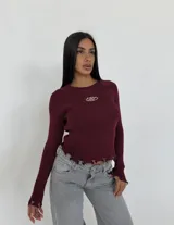 Sweater de tejido acanalado color bordó, con diseño entallado, mangas largas y terminaciones con efecto desgastado en el ruedo y los puños. Presenta un detalle bordado en el centro del pecho.