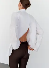 Camisa de algodón con diseño oversize y largo, cuello camisero clásico, cierre frontal con botones y mangas largas con puños abotonados. Presenta un diseño distintivo con espalda cruzada.