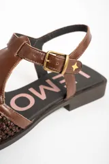 Sandalias de cuero marrón, con puntera cerrada de diseño trenzado, empeine liso y tira ajustable con hebilla en el talón. Cuenta con suela plana y baja.