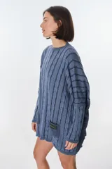 Sweater de tejido de punto con diseño de ochos, color beige, de corte holgado y manga larga con puños ajustados. Presenta dos bolsillos frontales tipo parche con detalle de etiqueta de cuero.