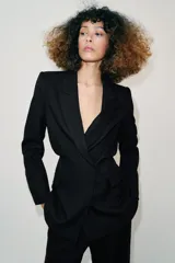 Blazer de cuello solapa y manga larga con hombreras marcadas. Presenta un diseño cruzado con cierre frontal de botones a presión, bolsillos delanteros con solapa y un detalle de cintura entallada con efecto abullonado.