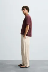 Pantalón de corte recto, color beige claro, con pliegues frontales y bolsillos de vivo en la parte trasera.