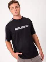 Remera negra de manga corta con diseño deportivo, parte superior de las mangas en color gris con ribete blanco y estampa frontal con la marca Rusty.