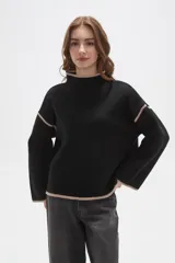 Polera de tejido de punto color negro con detalles de vivos en color beige en el cuello, puños, ruedo y costuras de las mangas. Presenta un diseño holgado con cuello alto y mangas largas.