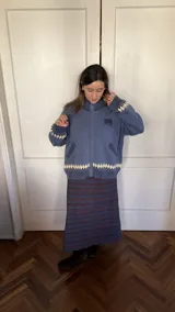 Saco tipo cardigan de punto jacquard color azul, con cierre frontal de aluminio. Presenta un diseño floral en la espalda y detalle de rombos en el ruedo y puños.