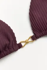 Corpiño de bikini negro, tipo triángulo, con textura acanalada y un detalle central metálico dorado con forma de moño o lazo.