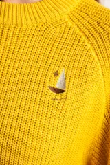 Sweater de punto en color amarillo, con diseño oversize, cuello redondo y manga larga. Presenta un pequeño bordado de un velero en la parte superior del pecho.
