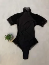 Body de lycra color negro con cuello alto, mangas cortas de microtul y detalles de encaje en el cuello, mangas y laterales. Presenta un diseño entallado con espalda descubierta.