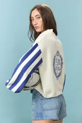 Cardigan de algodón color azul con mangas largas de rayas verticales anchas en tonos azul y celeste, puños en rojo, y bordado en la espalda con diseño de escudo nacional.