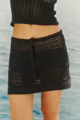 Falda corta de tejido de punto calado en color negro, con diseño de cintura baja y lazo ajustable en la cintura.