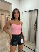 Short de cuero sintético negro con cierre frontal de doble botón, detalle de tachas metálicas en forma de osito en los bolsillos delanteros y ojales metálicos laterales.